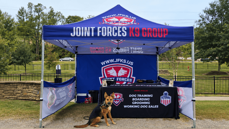 A promotional tent for Joint Forces K9 Group with a dog sitting in front