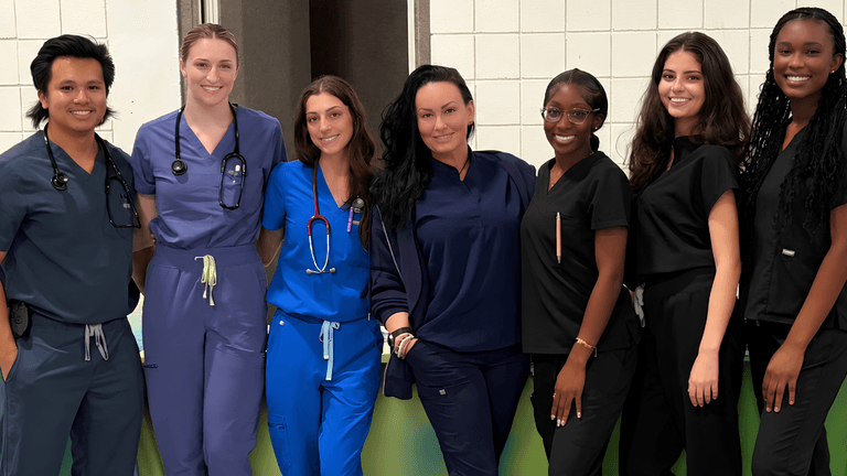 Group of seven healthcare professionals posing together in scrubs and medical attire