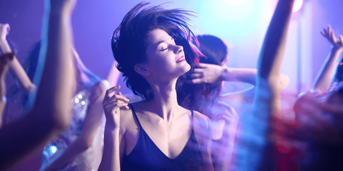 A woman dancing joyfully in a vibrant, colorful party atmosphere with swirling lights