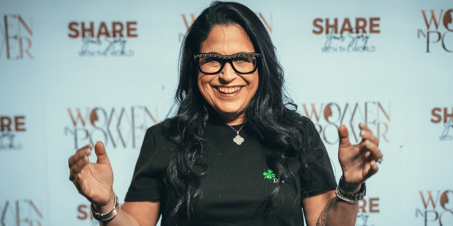 Smiling woman with glasses standing in front of a women empowerment backdrop