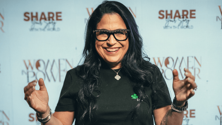 Smiling woman with glasses standing in front of a women empowerment backdrop