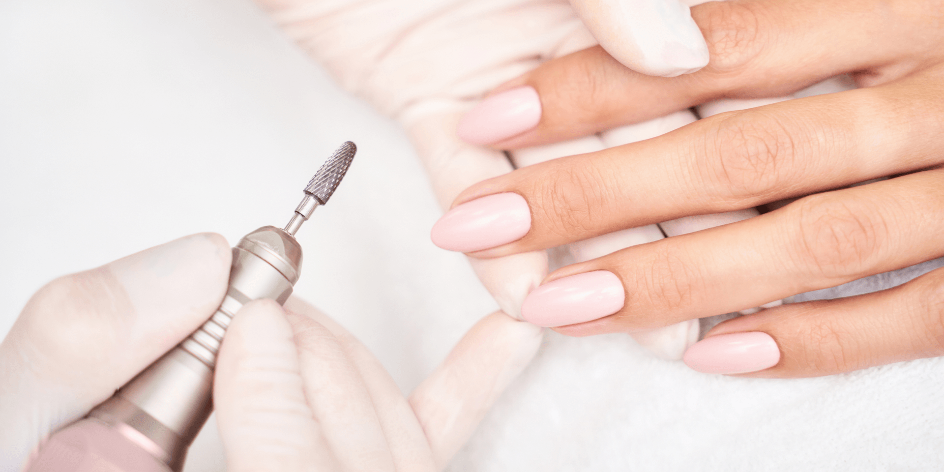 A nail technician shaping pink manicured nails with an electric file.