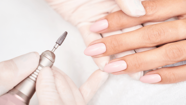 A nail technician shaping pink manicured nails with an electric file.