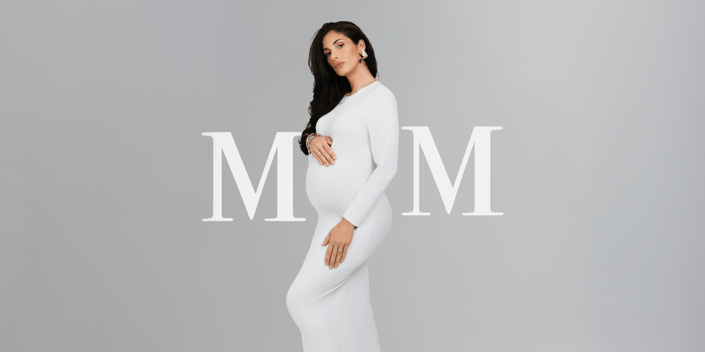 Pregnant woman in a white dress poses stylishly against a neutral background