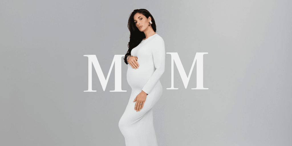 Pregnant woman in a white dress poses stylishly against a neutral background