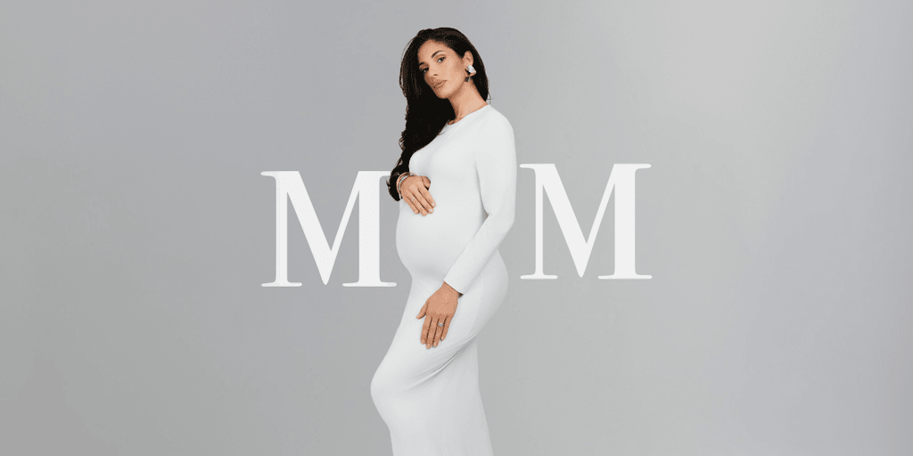 Pregnant woman in a white dress poses stylishly against a neutral background