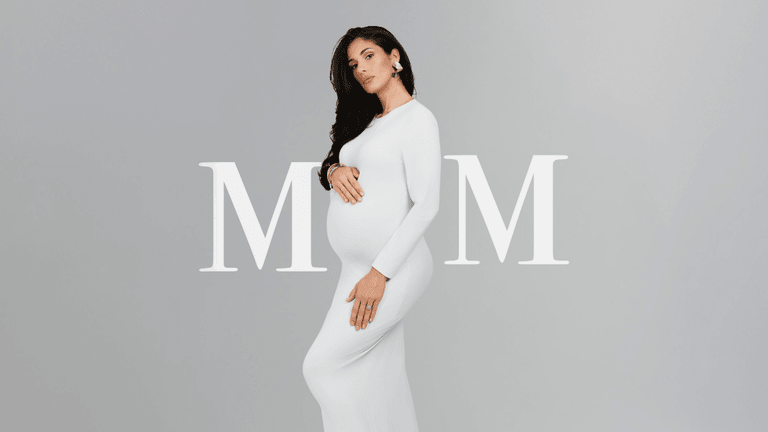 Pregnant woman in a white dress poses stylishly against a neutral background