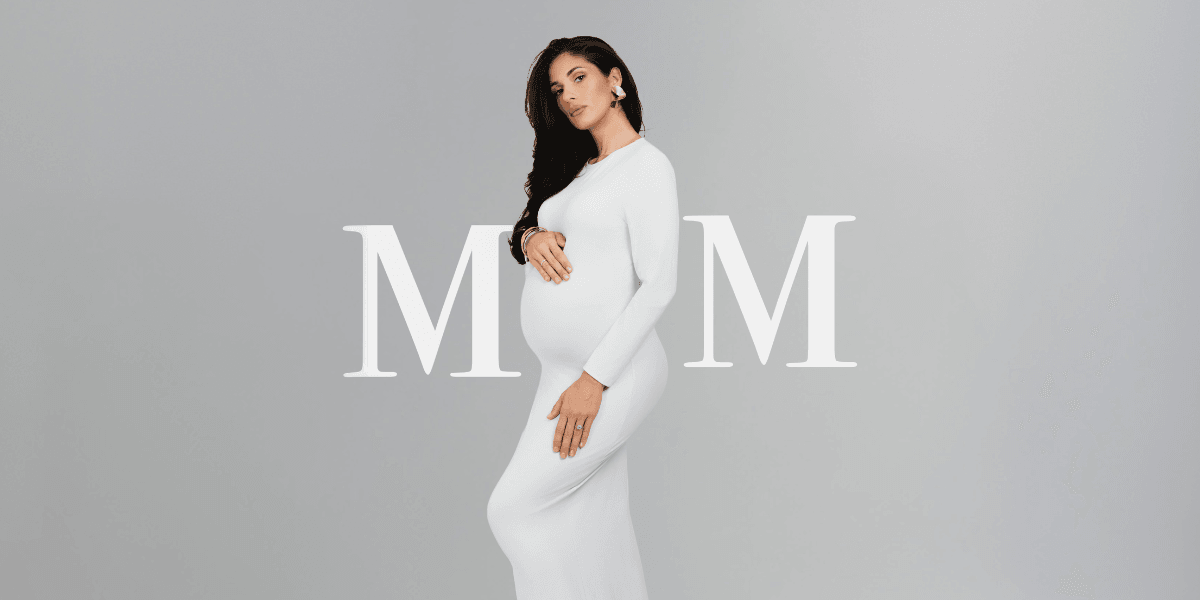 Pregnant woman in a white dress poses stylishly against a neutral background