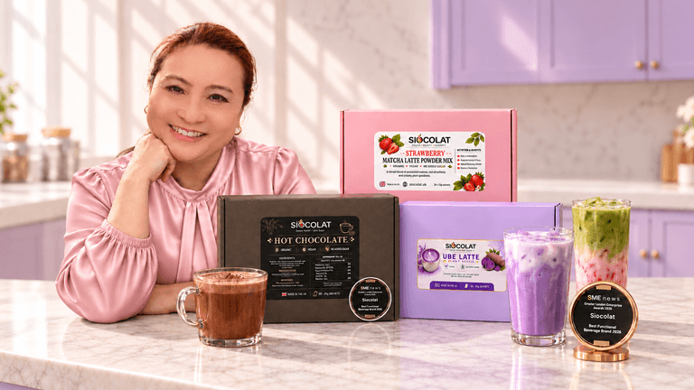 Woman smiling behind various colorful beverage products on a kitchen counter.