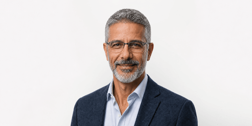 Middle-aged man with grey hair and glasses, wearing a blue suit jacket and white shirt
