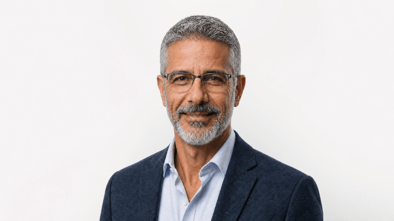 Middle-aged man with grey hair and glasses, wearing a blue suit jacket and white shirt