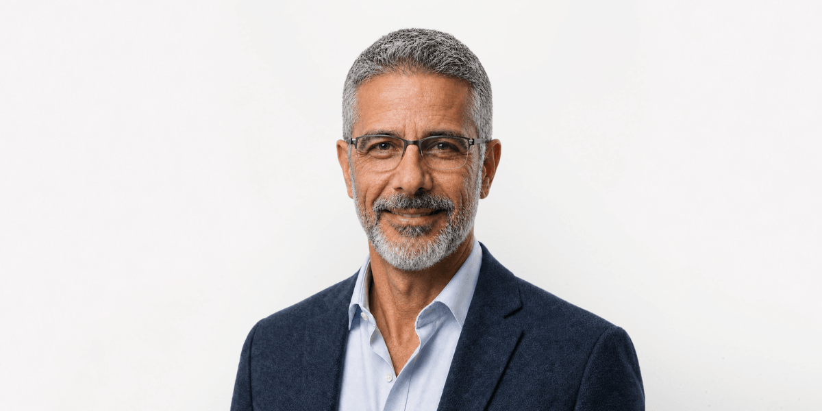 Middle-aged man with grey hair and glasses, wearing a blue suit jacket and white shirt
