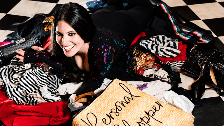 A woman lies on a colorful pile of clothes, smiling with a stylish background.