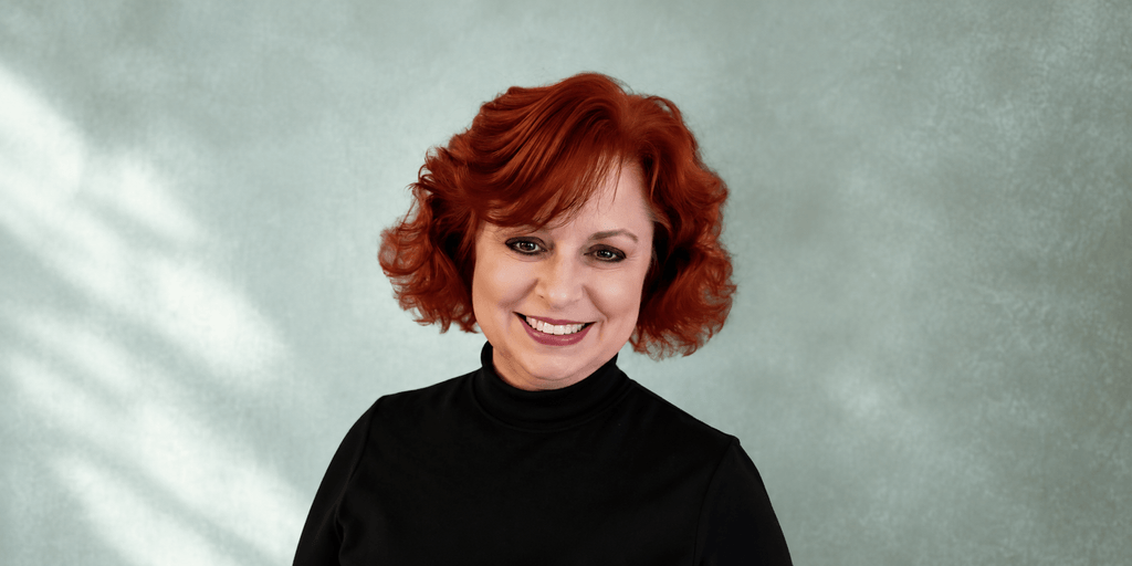 Woman with curly red hair smiling against a soft, textured green background