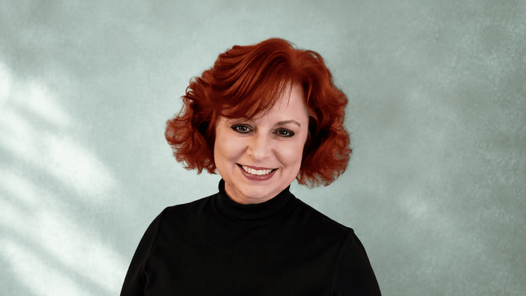Woman with curly red hair smiling against a soft, textured green background