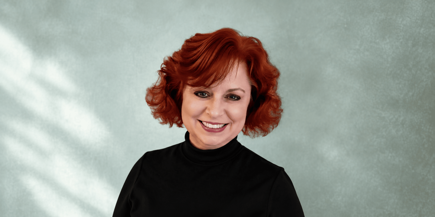 Woman with curly red hair smiling against a soft, textured green background