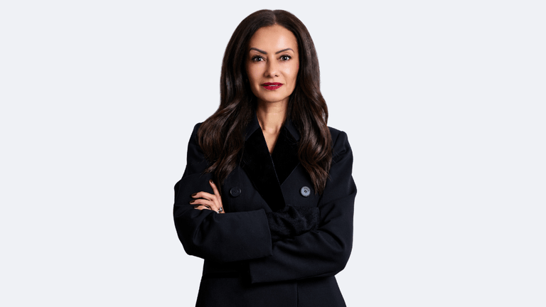 Woman with long dark hair wearing a black coat, arms crossed confidently
