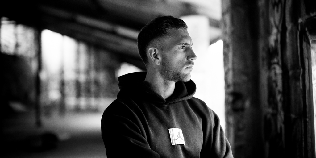 Young man in a black hoodie gazes thoughtfully in a graffiti-filled space