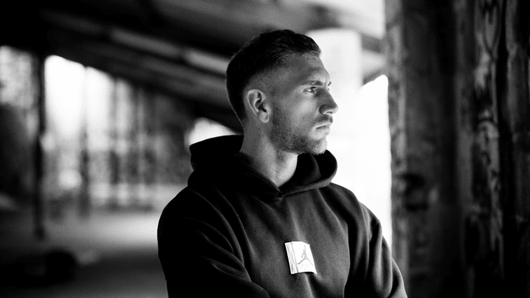 Young man in a black hoodie gazes thoughtfully in a graffiti-filled space
