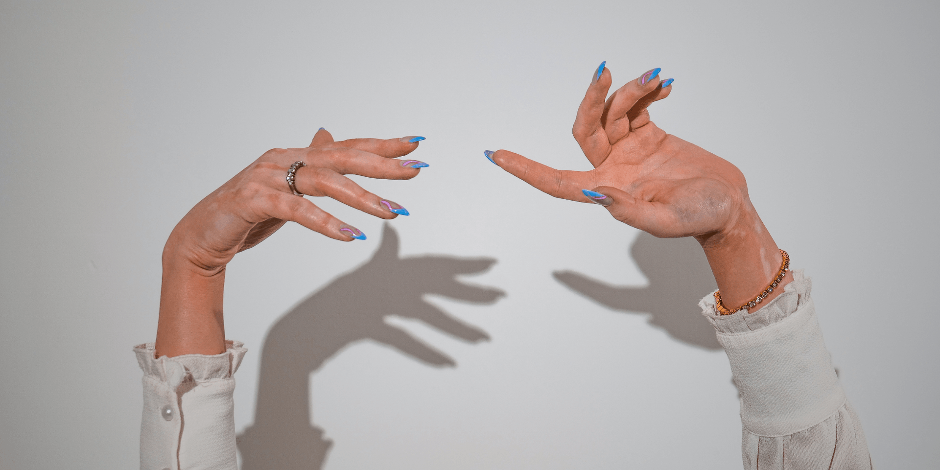 Two hands with stylish blue nails reaching outward, casting shadows against a white background