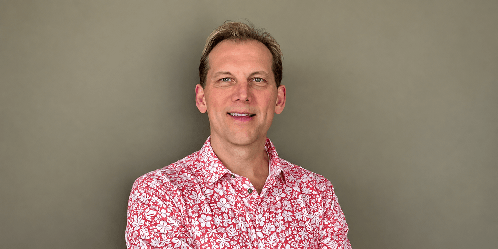 Smiling man in a floral shirt posing with arms crossed against a neutral background