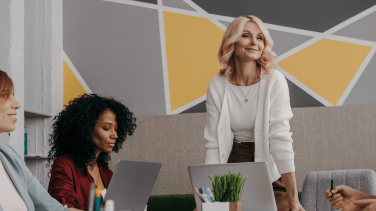 Four women in a modern workspace with laptops, engaged in a discussion.