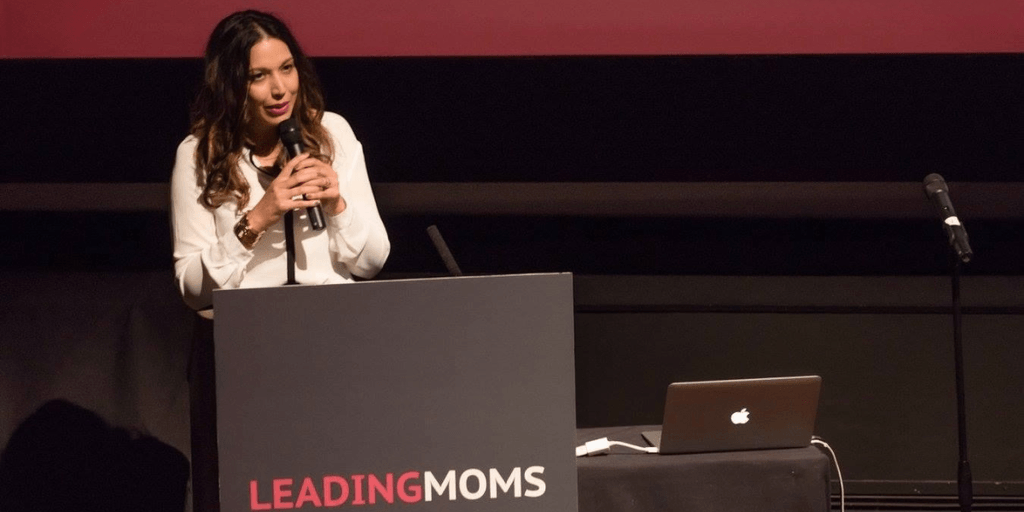 A woman speaks at a podium during the Leading Moms event, with a laptop nearby