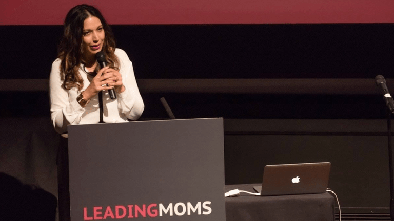 A woman speaks at a podium during the Leading Moms event, with a laptop nearby
