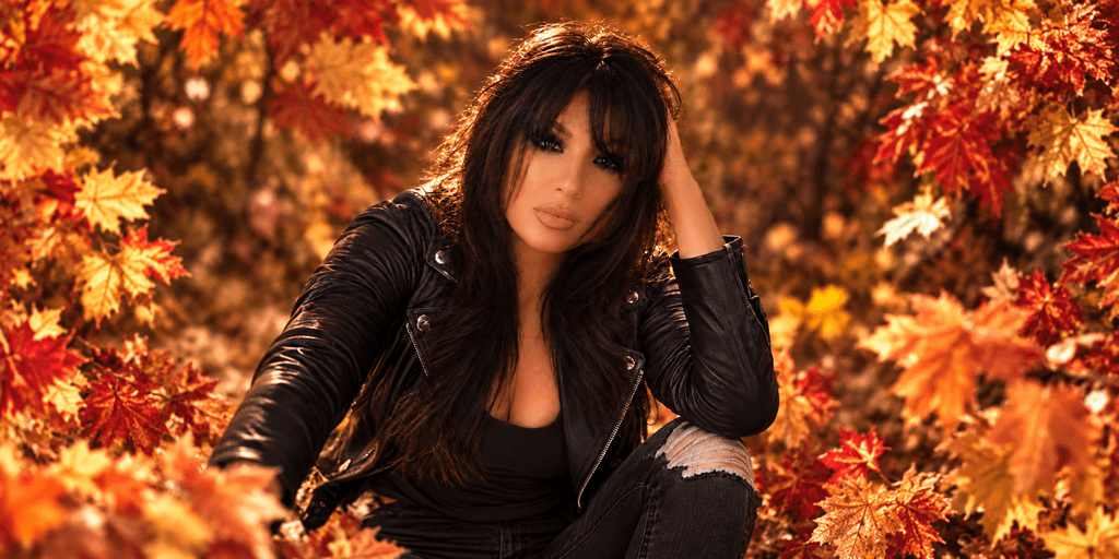 A woman in a black leather jacket sits among vibrant autumn leaves.