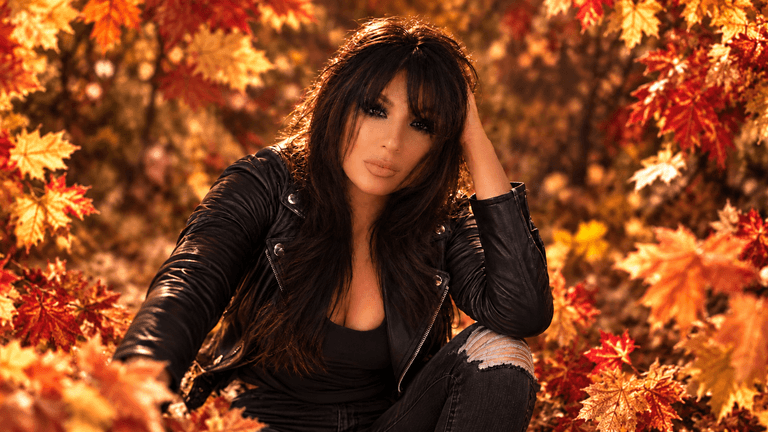 A woman in a black leather jacket sits among vibrant autumn leaves.