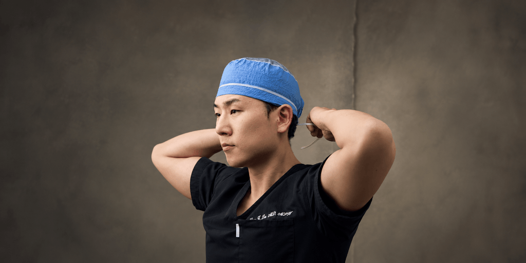 A surgeon in scrubs adjusts a blue surgical cap before an operation