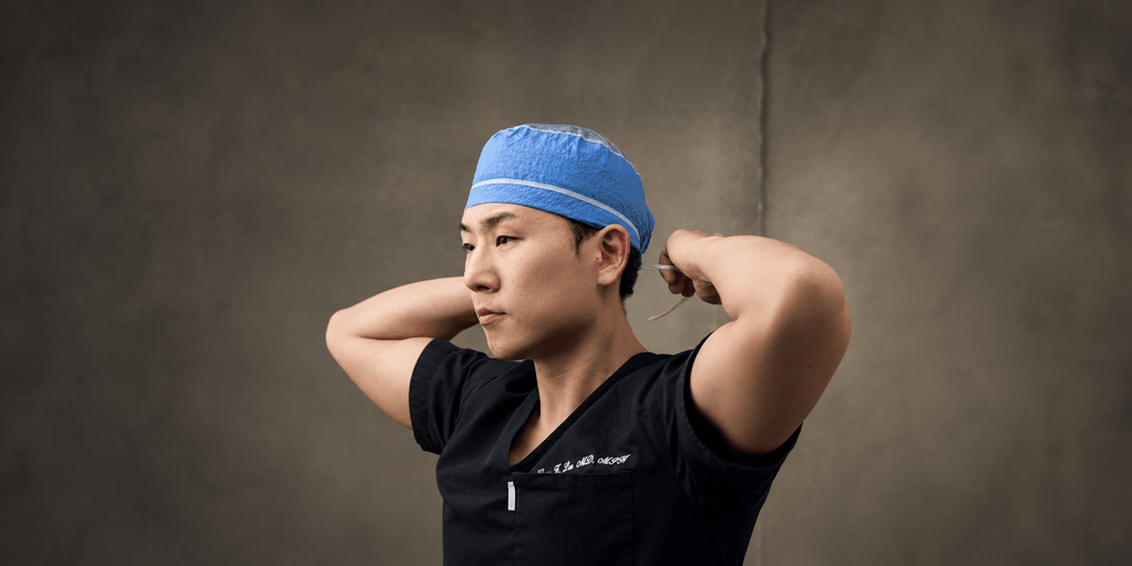 A surgeon in scrubs adjusts a blue surgical cap before an operation