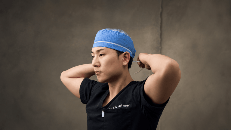 A surgeon in scrubs adjusts a blue surgical cap before an operation