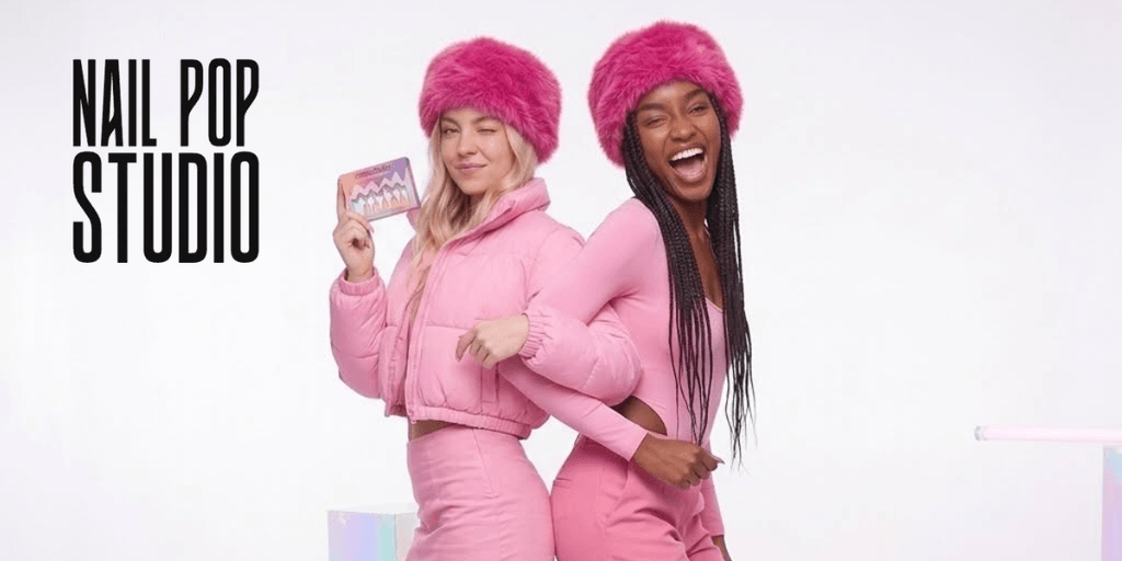 Two models in pink outfits and fluffy hats posing playfully against a white background