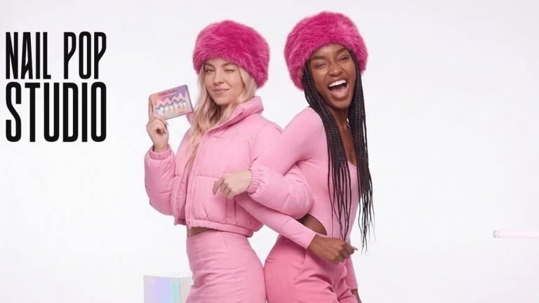 Two models in pink outfits and fluffy hats posing playfully against a white background
