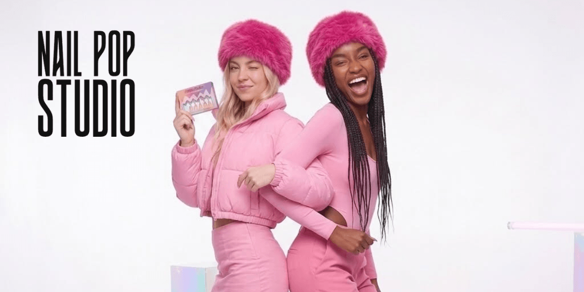 Two models in pink outfits and fluffy hats posing playfully against a white background