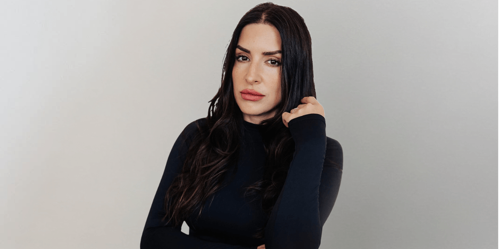 Woman with long dark hair wearing a black fitted top poses against a neutral background