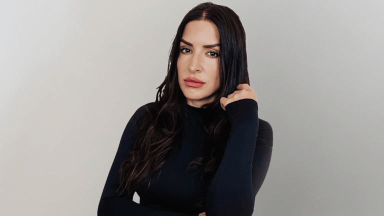 Woman with long dark hair wearing a black fitted top poses against a neutral background