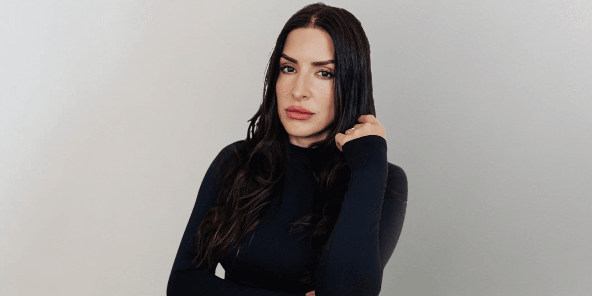 Woman with long dark hair wearing a black fitted top poses against a neutral background