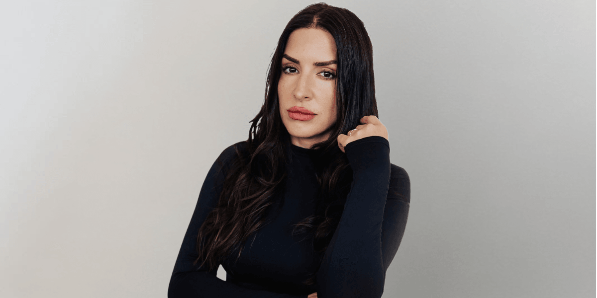 Woman with long dark hair wearing a black fitted top poses against a neutral background