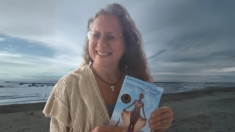 Woman smiling while holding a book by the beach under a cloudy sky