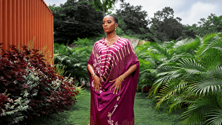 A woman in a vibrant purple outfit stands amid lush greenery and colorful plants