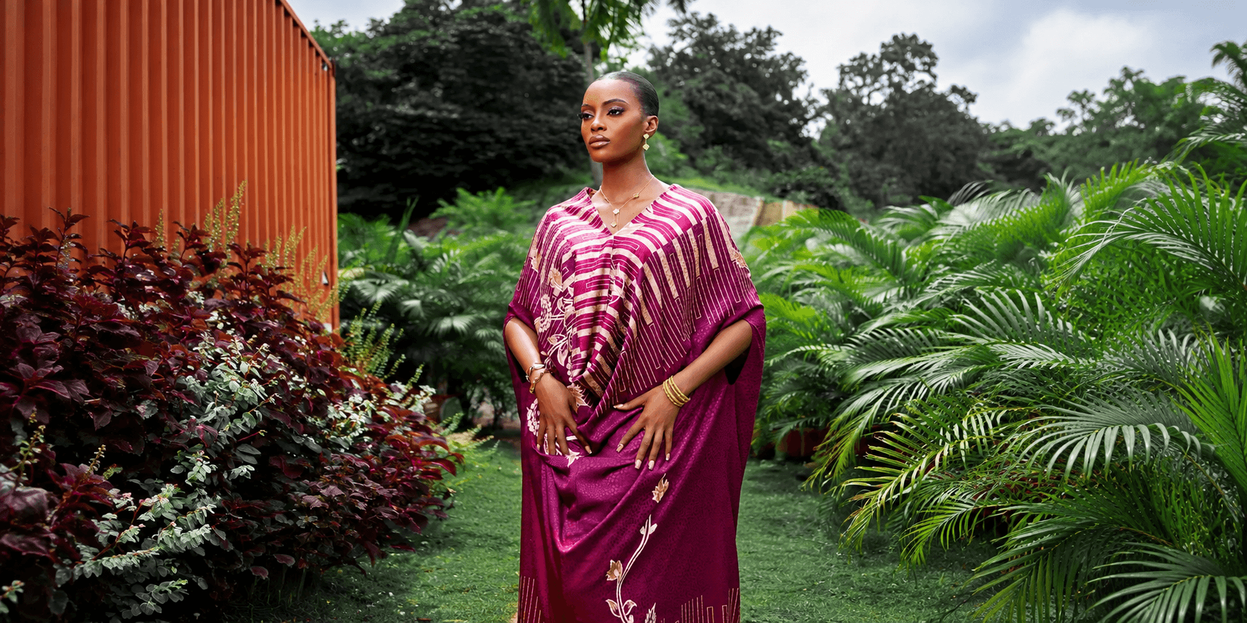 A woman in a vibrant purple outfit stands amid lush greenery and colorful plants