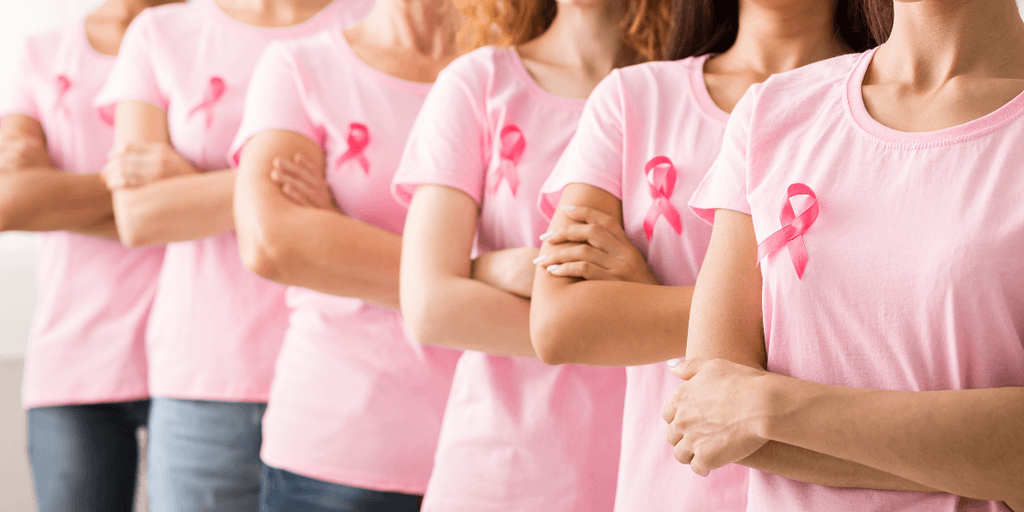 Women in pink shirts with pink ribbons standing in a row with arms crossed