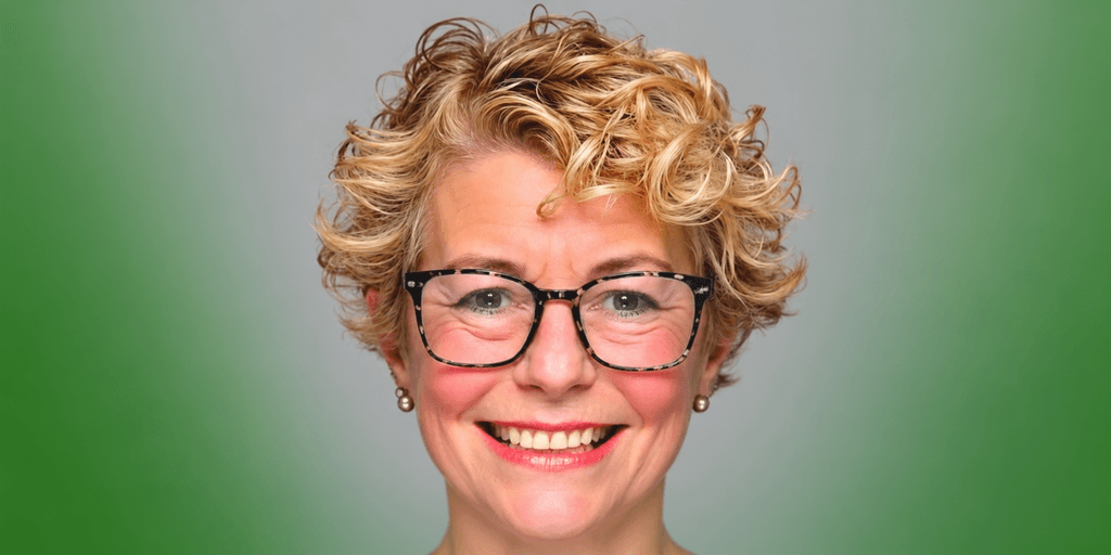 Smiling woman with short curly hair and glasses against a gradient green background