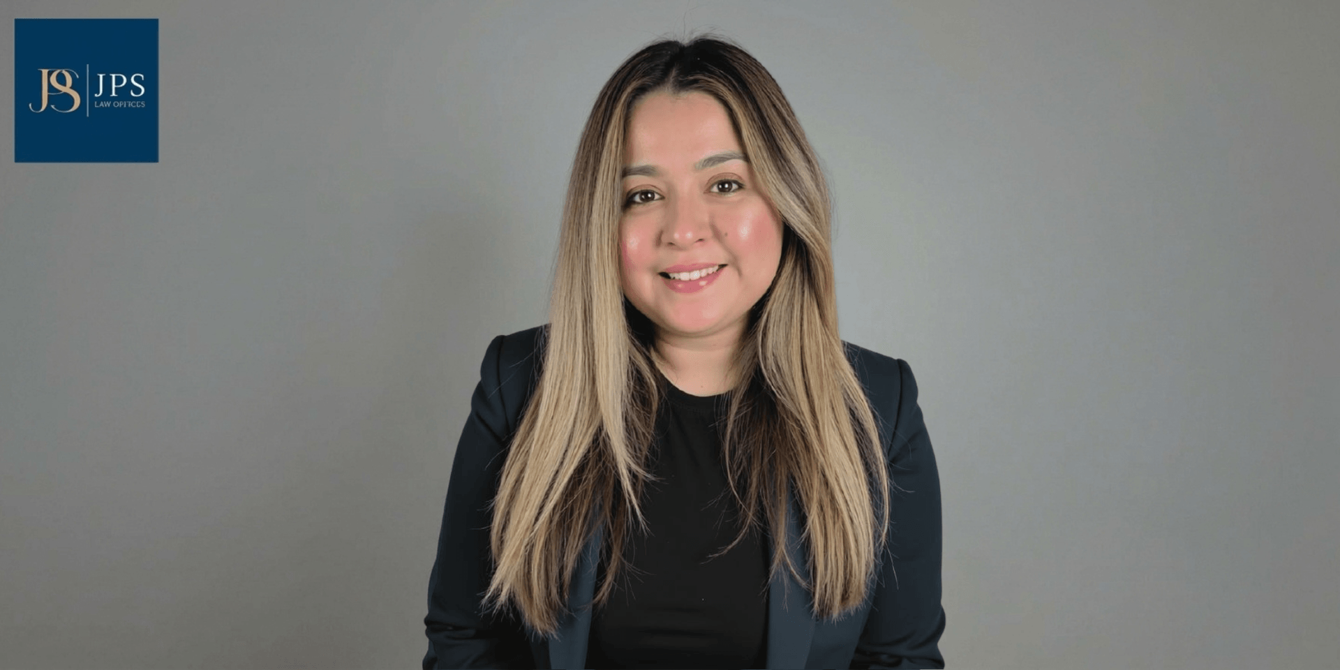 Smiling woman with long hair in a blazer against a light gray background