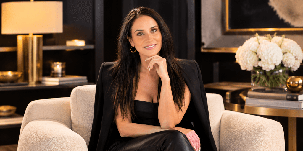 A woman with long dark hair smiles while seated on a couch in a stylish room