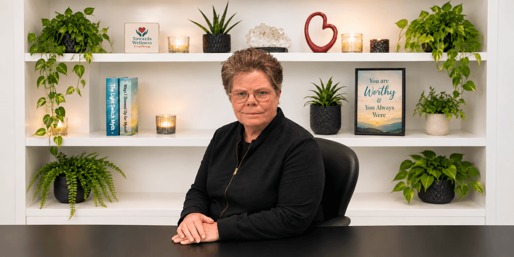 A woman sits at a desk in front of a well-decorated shelf with plants.