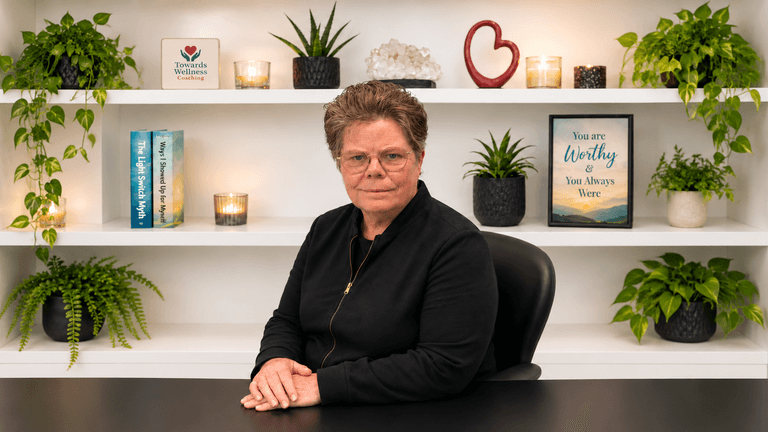 A woman sits at a desk in front of a well-decorated shelf with plants.