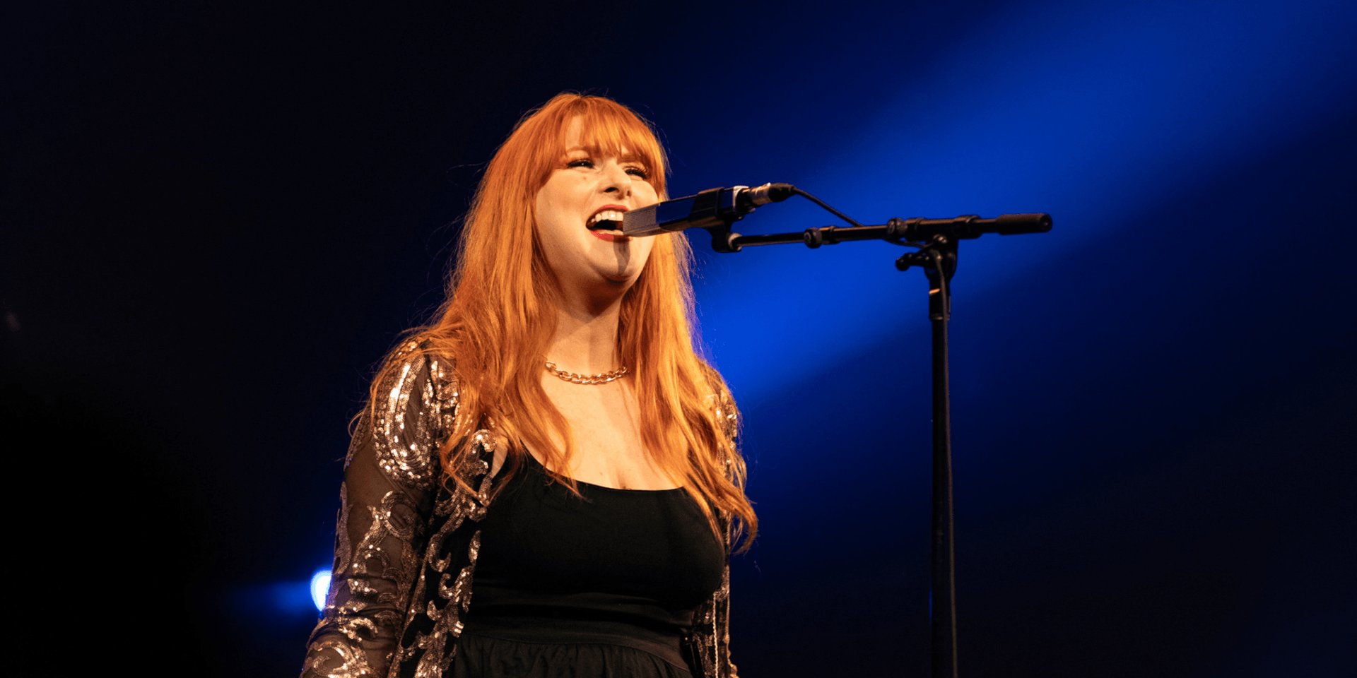 A woman with long red hair sings passionately into a microphone on stage